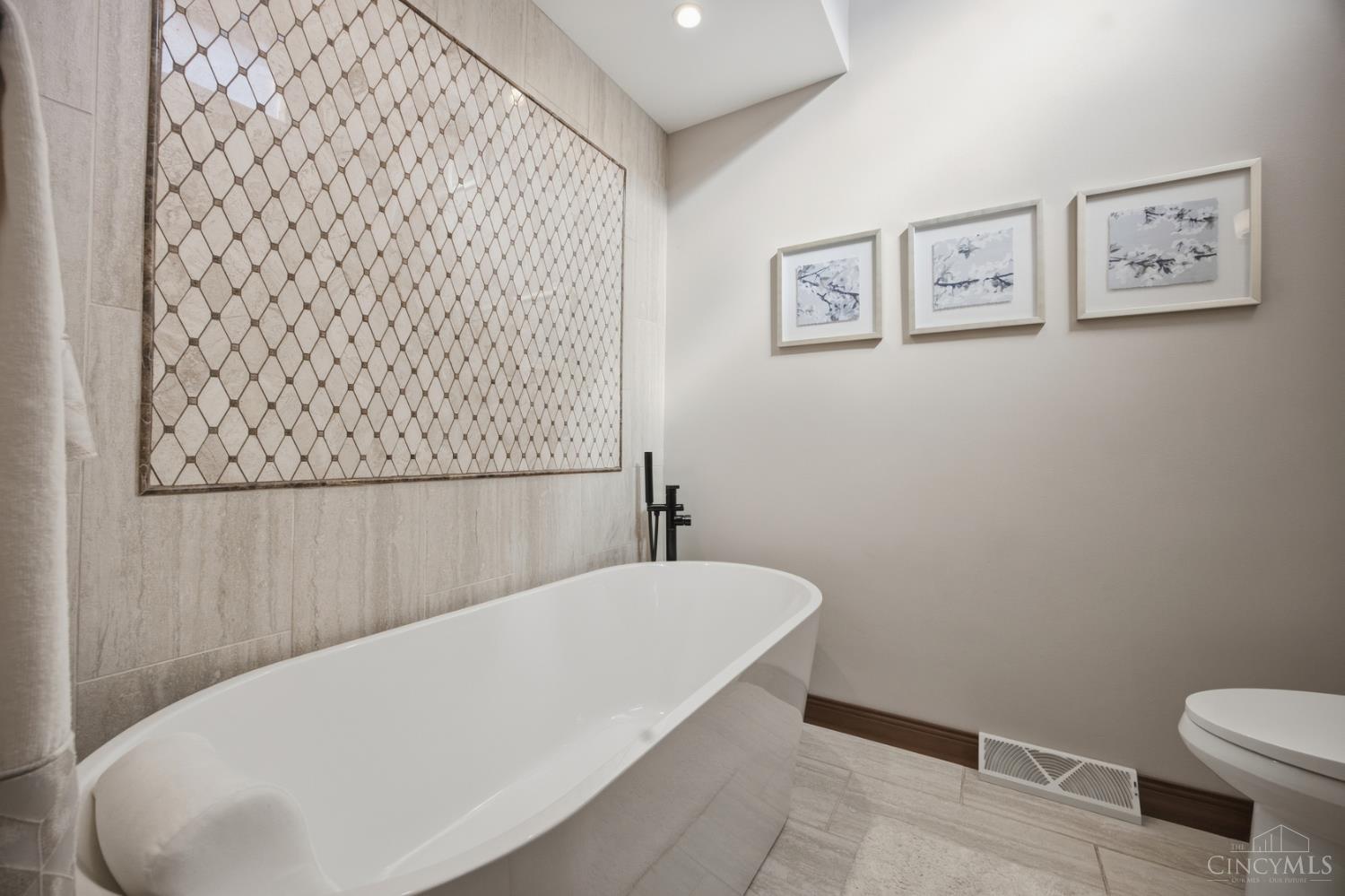 Bathroom with a freestanding tub, geometric tile accent wall, and black floor-mounted faucet.