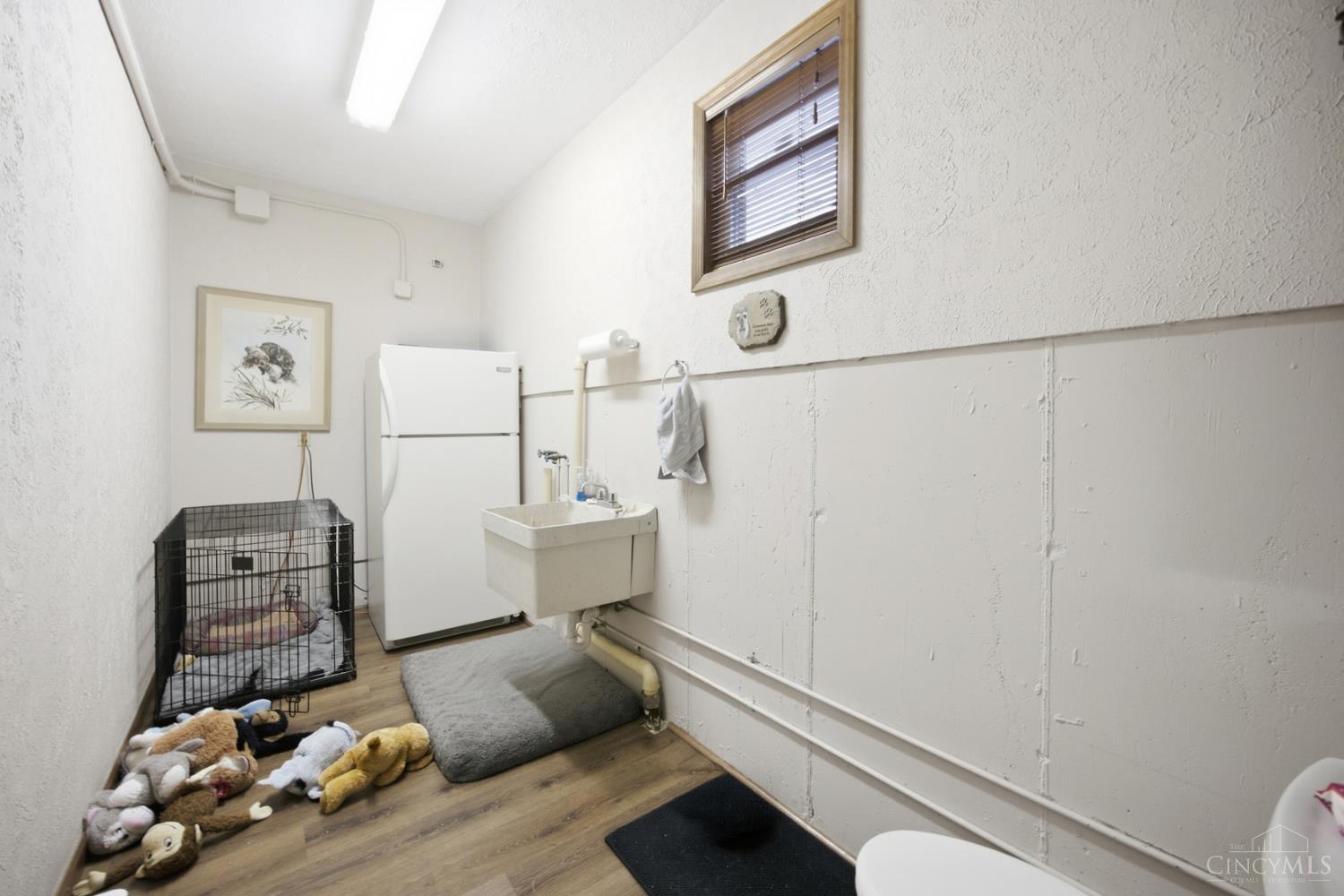 Utility room with a deep sink, refrigerator, and pet crate with toys.