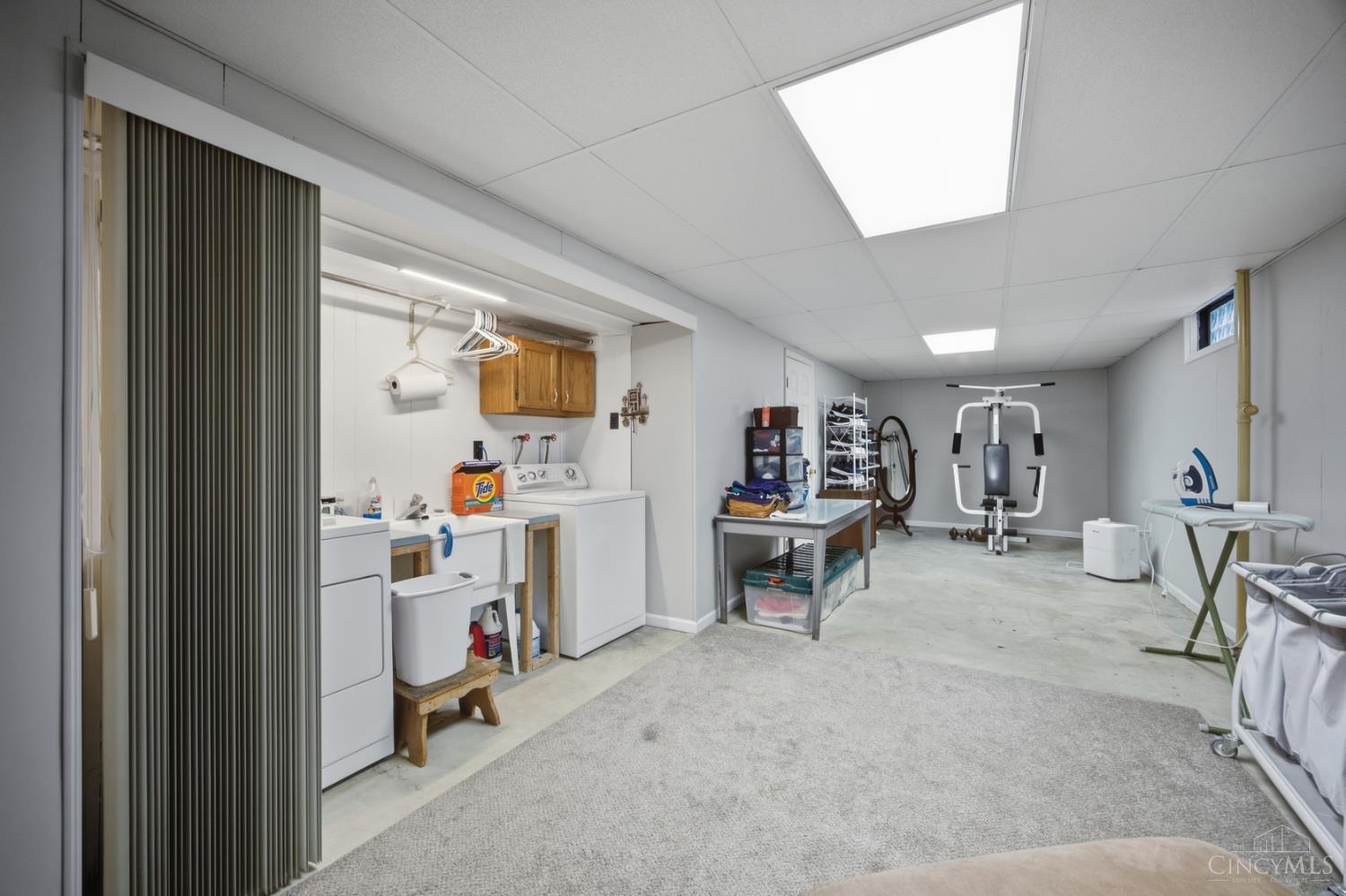 Finished basement with laundry appliances, a utility sink, exercise equipment, and an open carpeted area.