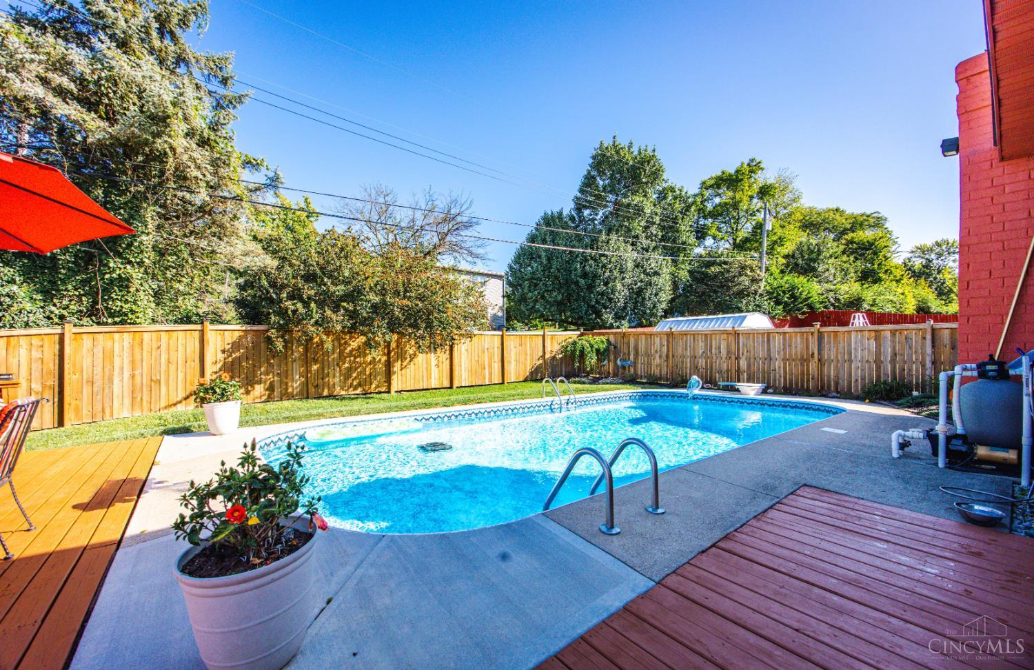 Backyard swimming pool with curved deck, wooden privacy fence, and red-brick house.