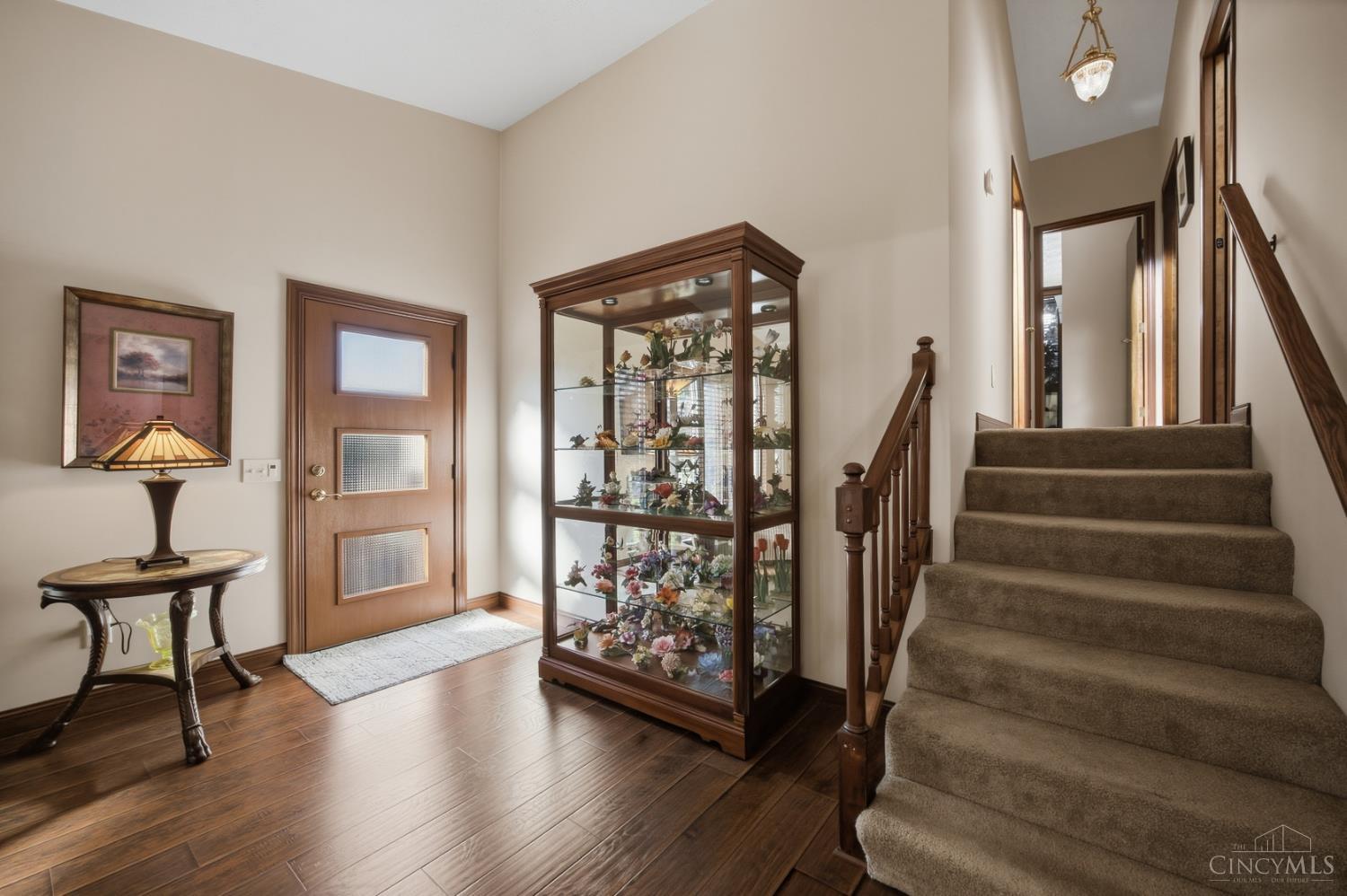 Furnished entryway with a glass display cabinet beside a carpeted staircase.