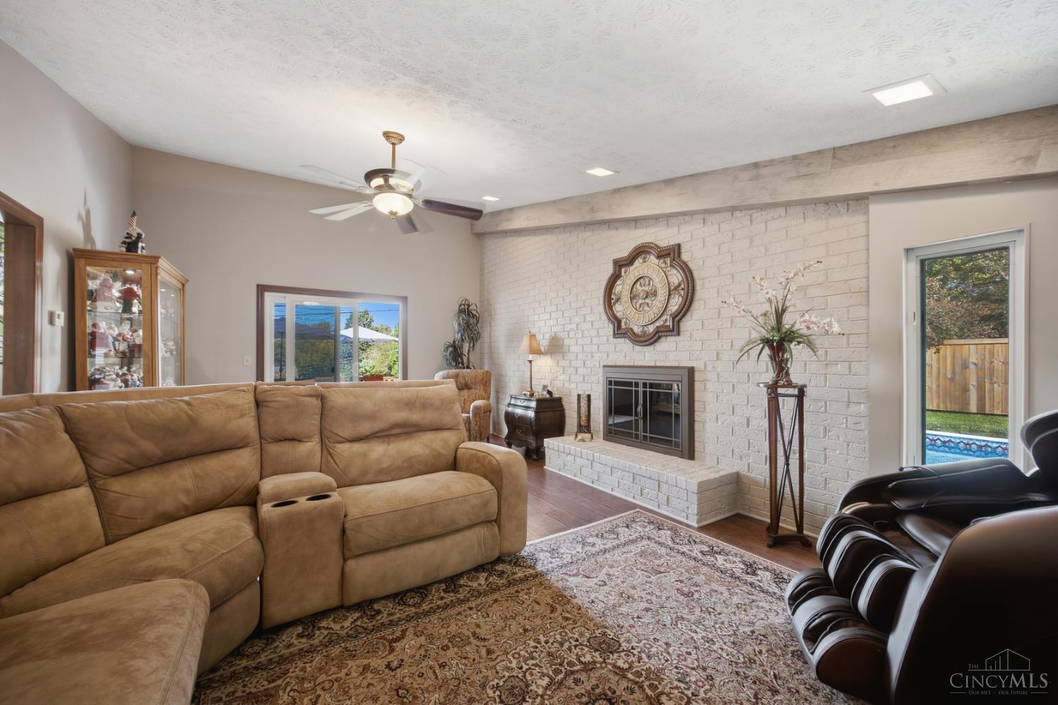 Living room with a white brick fireplace, tan sectional, dark leather recliners, and glass door overlooking the pool.