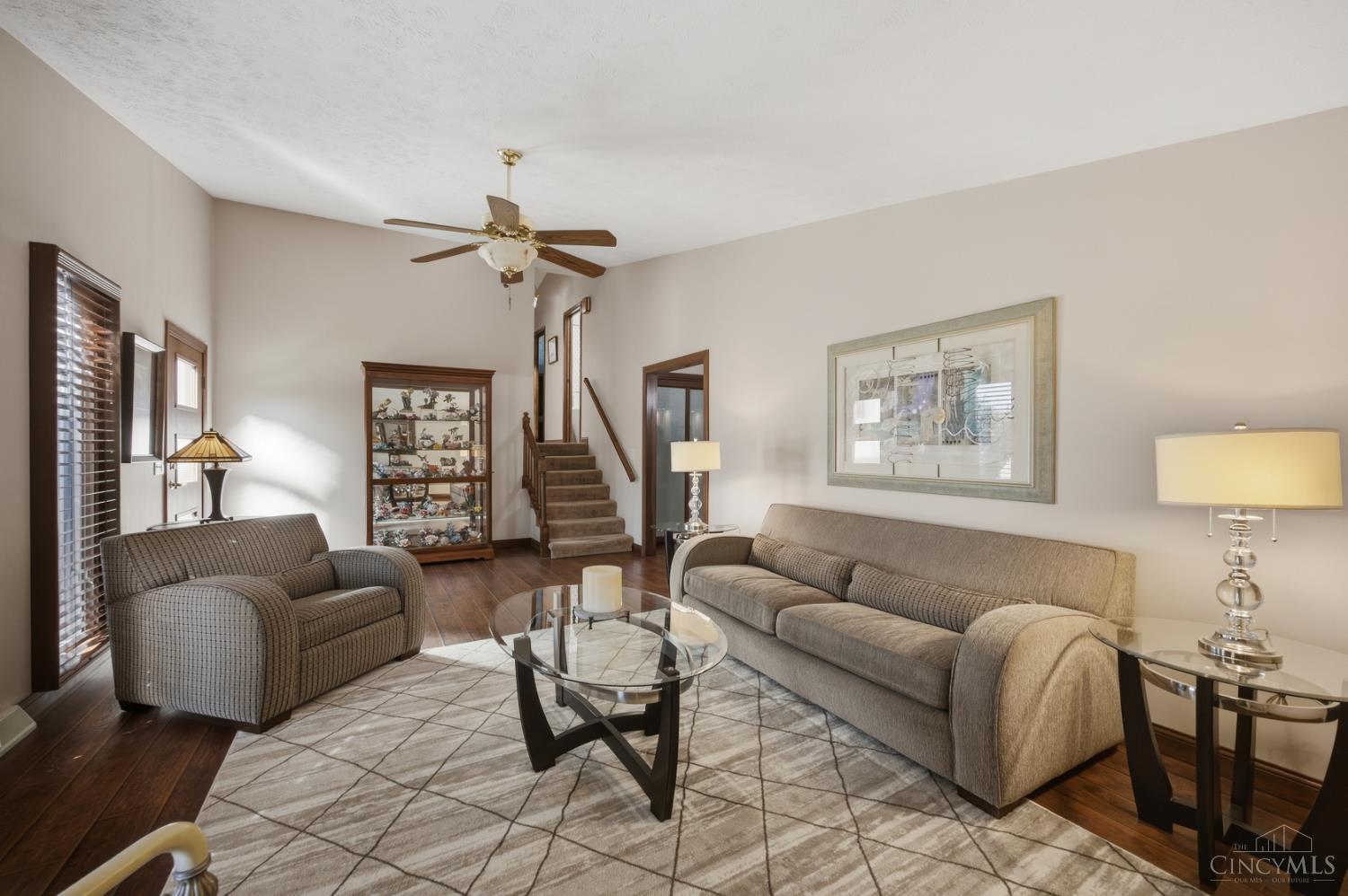 Furnished living room with gray seating, a glass coffee table, geometric rug, and staircase.