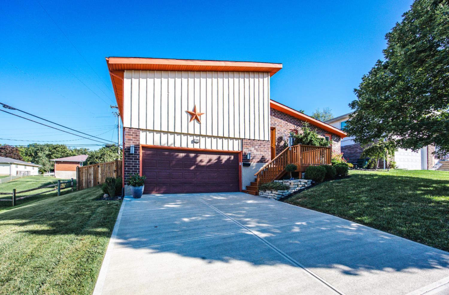 House exterior with a wide concrete driveway, dark double garage door, and wooden front deck.