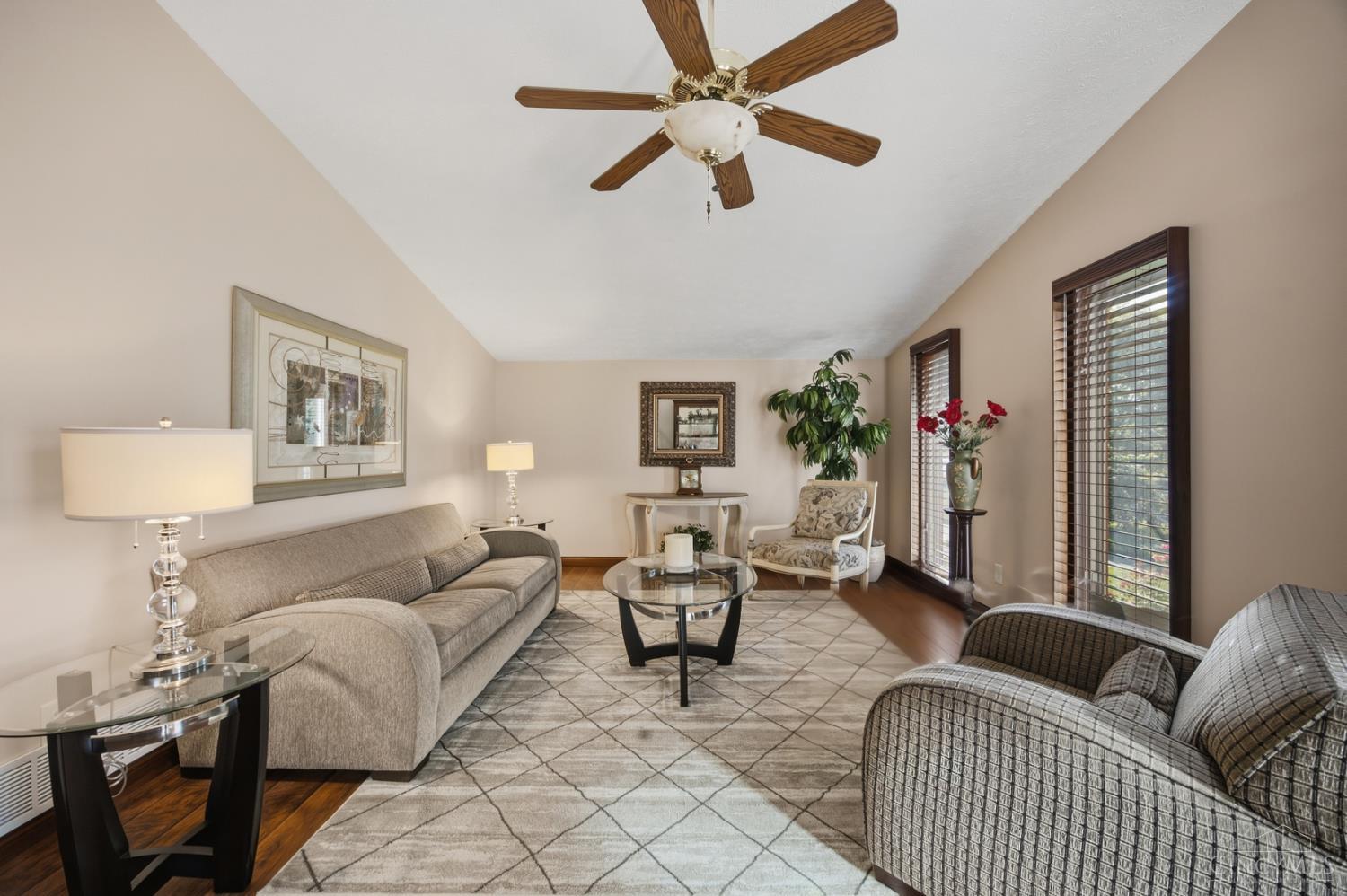 Furnished living room with a beige sofa, patterned armchairs, geometric rug, and tall windows with blinds.