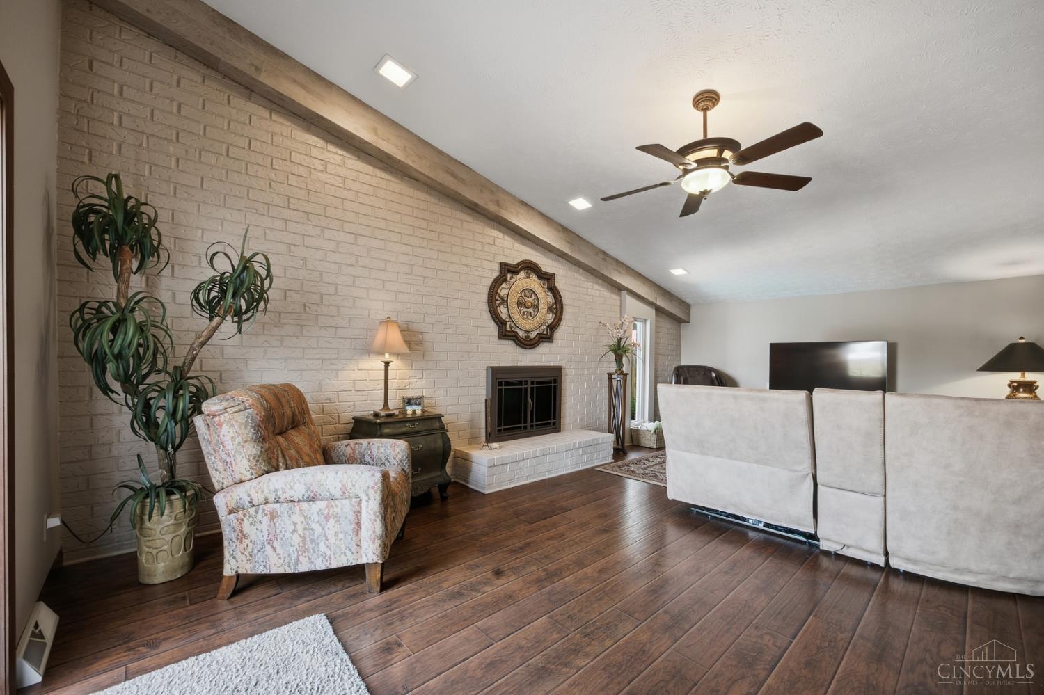 Furnished living room with a white brick fireplace, sloped wood-beam ceiling, and dark wood floors.