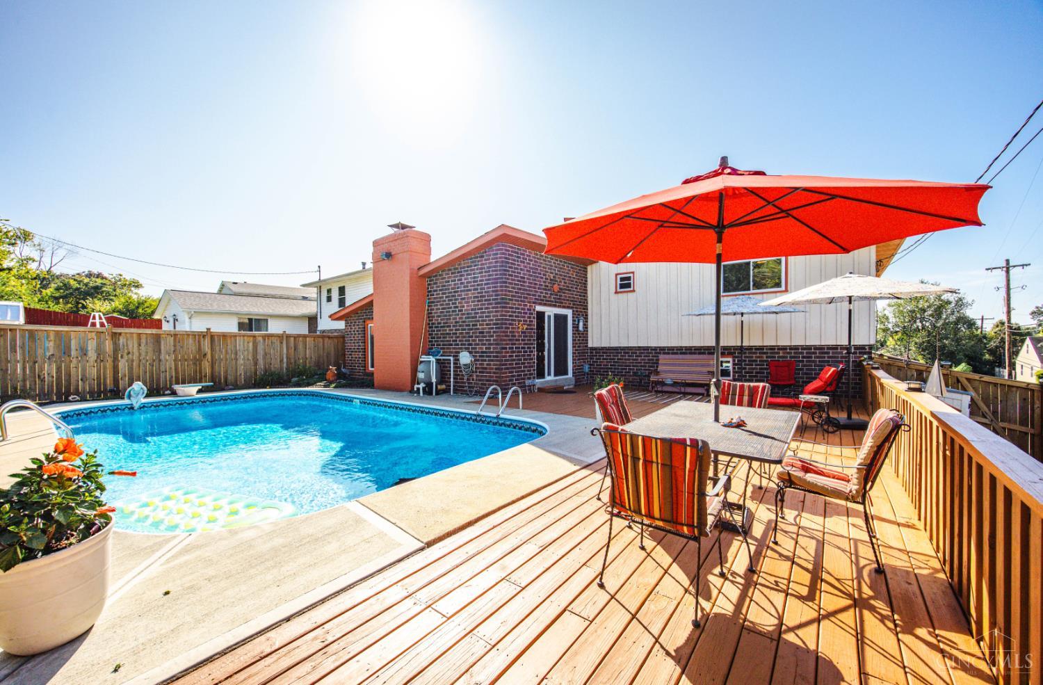 Backyard pool beside a furnished wooden deck shaded by a large red umbrella.