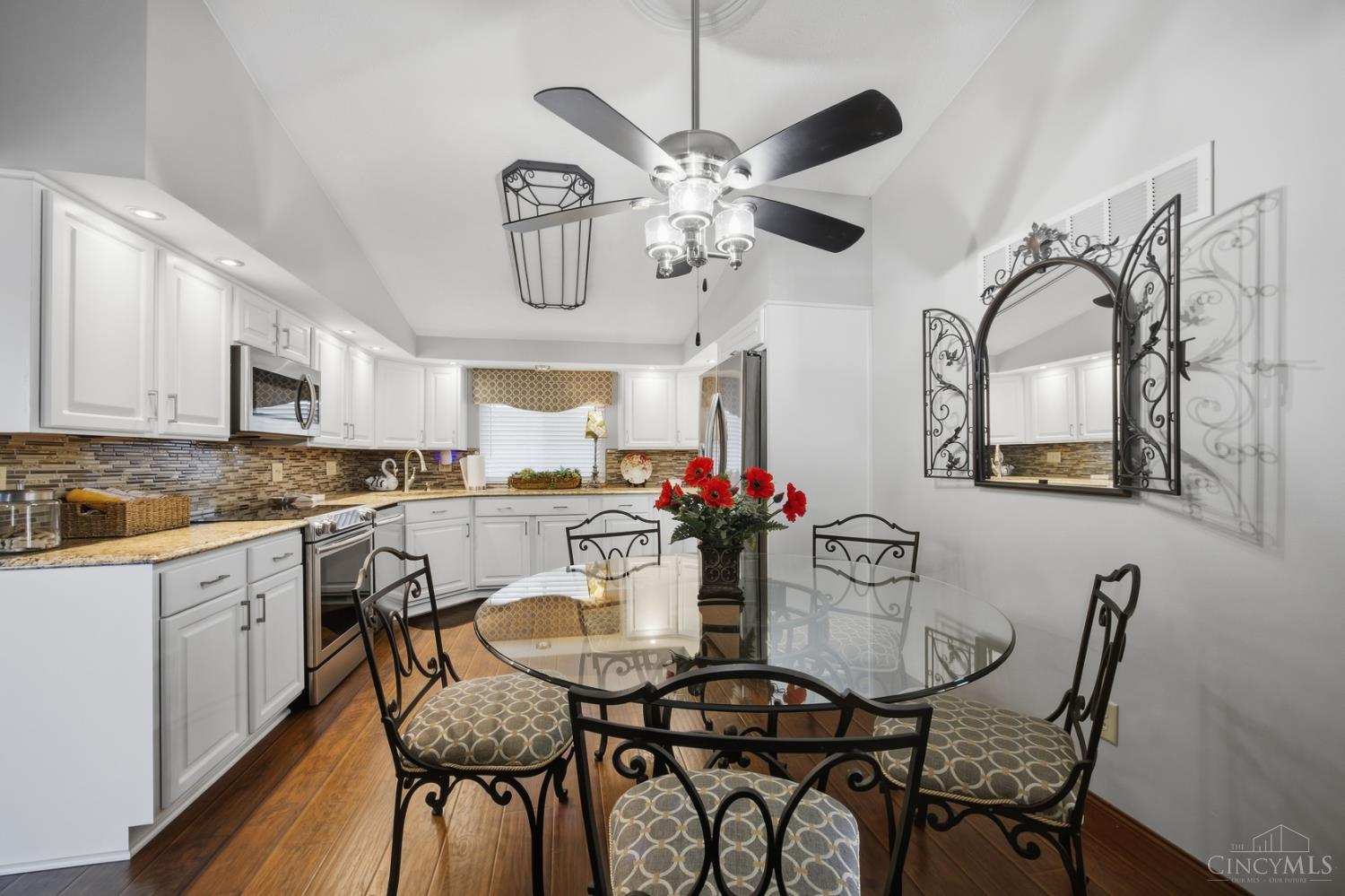 Kitchen and dining area with white cabinets, stainless appliances, and a glass table with ornate chairs.
