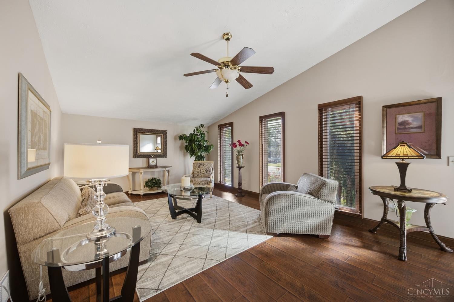 Living room with beige seating, hardwood floors, and tall windows with wooden blinds.