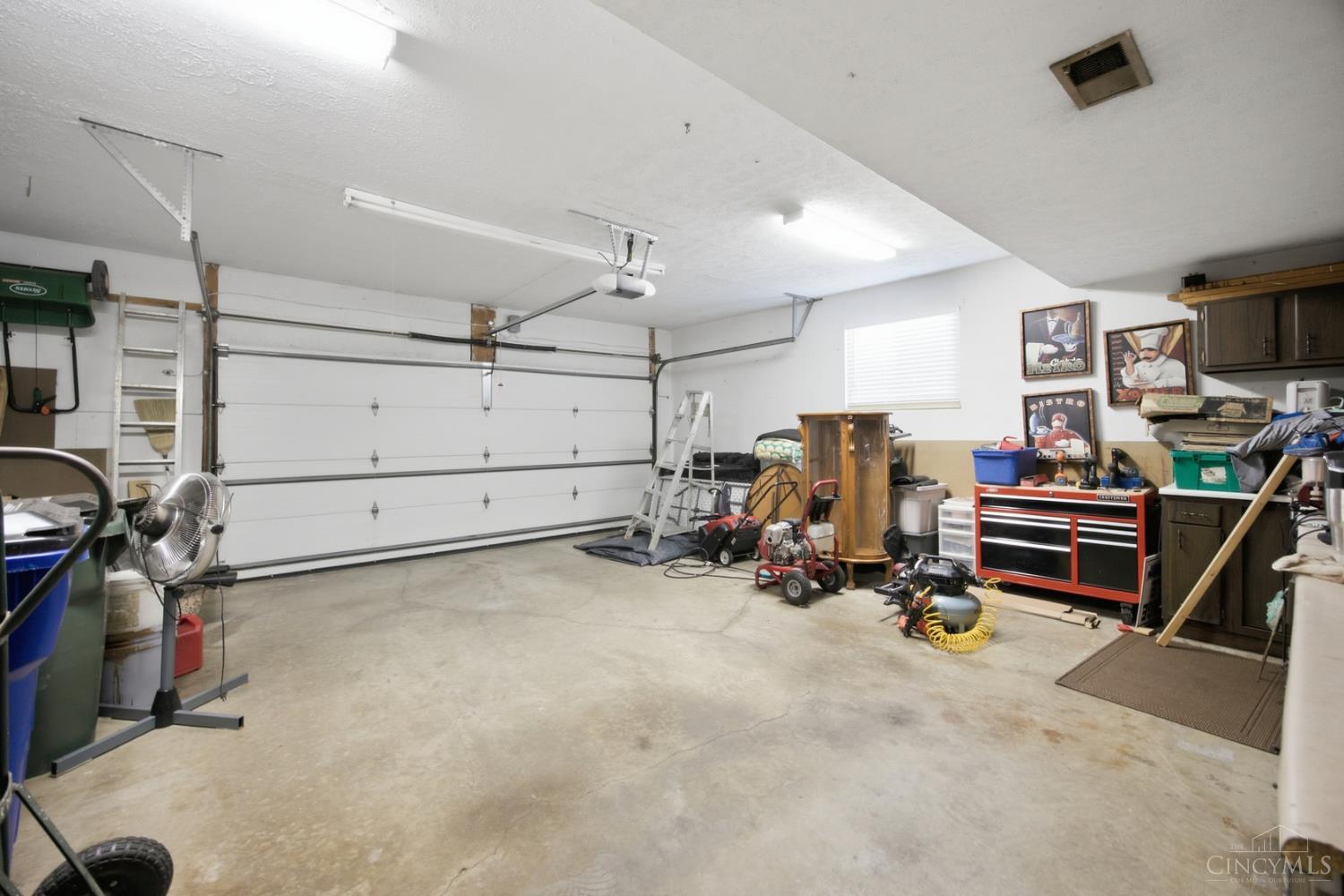 Spacious garage with a wide white door, concrete floor, and a tool-filled work area.