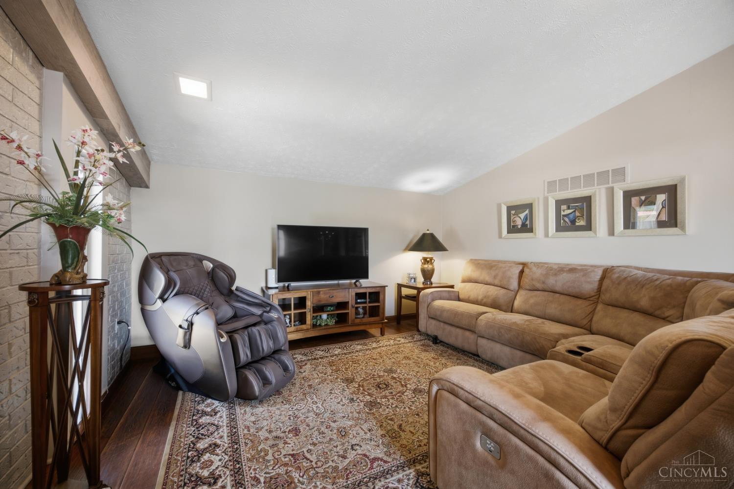 Living room with a tan sectional, patterned rug, massage chair, and brick fireplace.