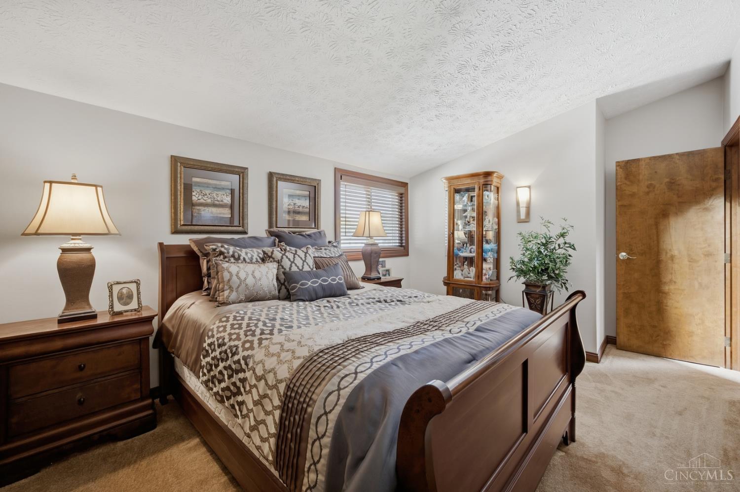 Furnished bedroom with a large dark wood bed, patterned bedding, and a glass-front display cabinet.