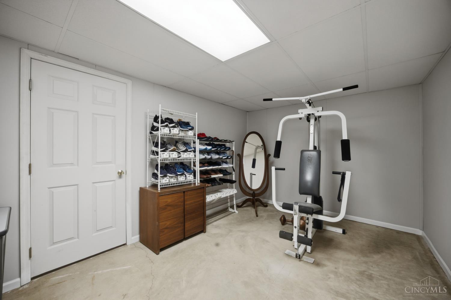 Home gym with a multi-gym weight machine, shoe racks, and a standing mirror.