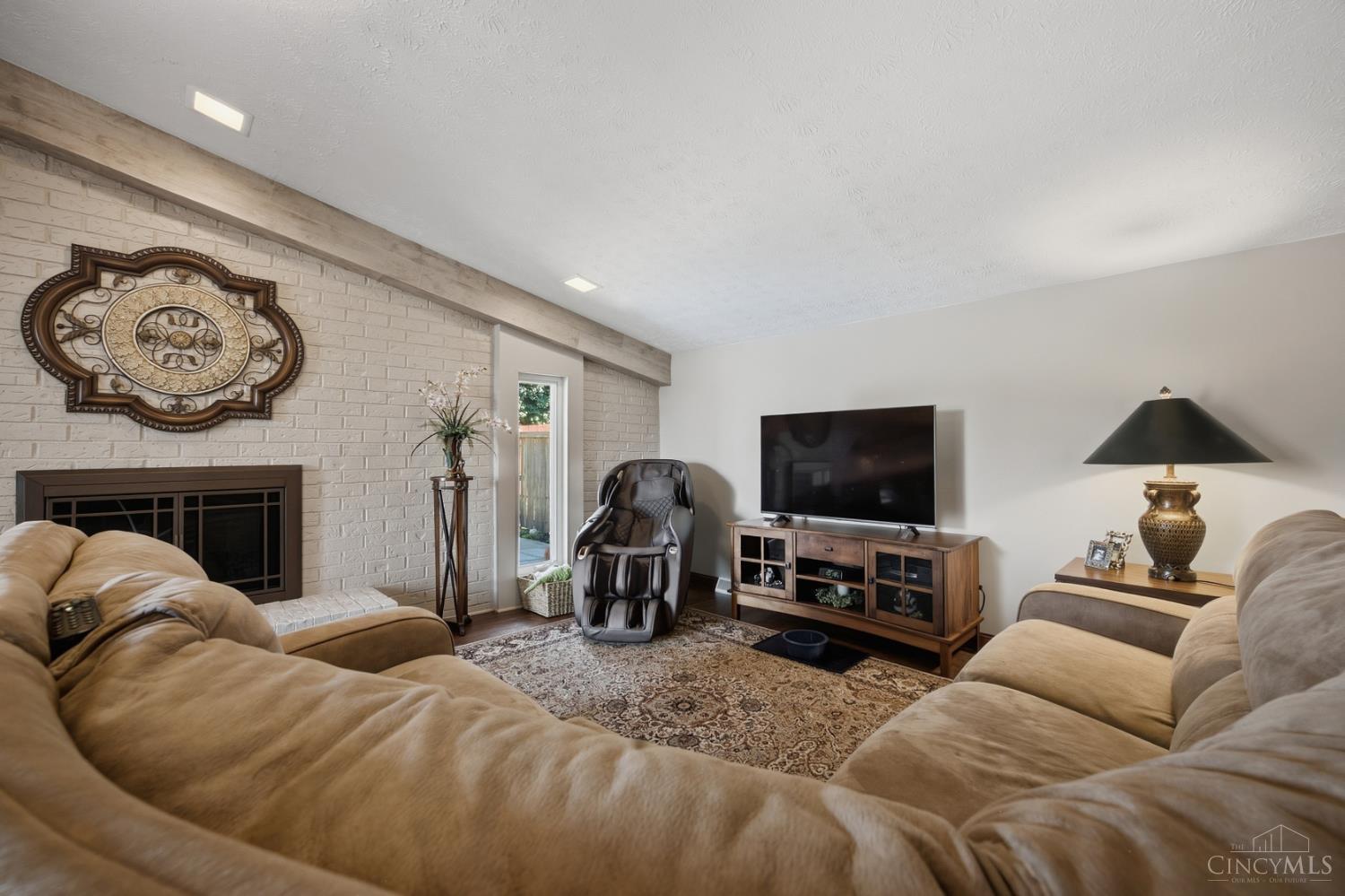 Furnished living room with a tan sectional, white brick fireplace, and massage chair.