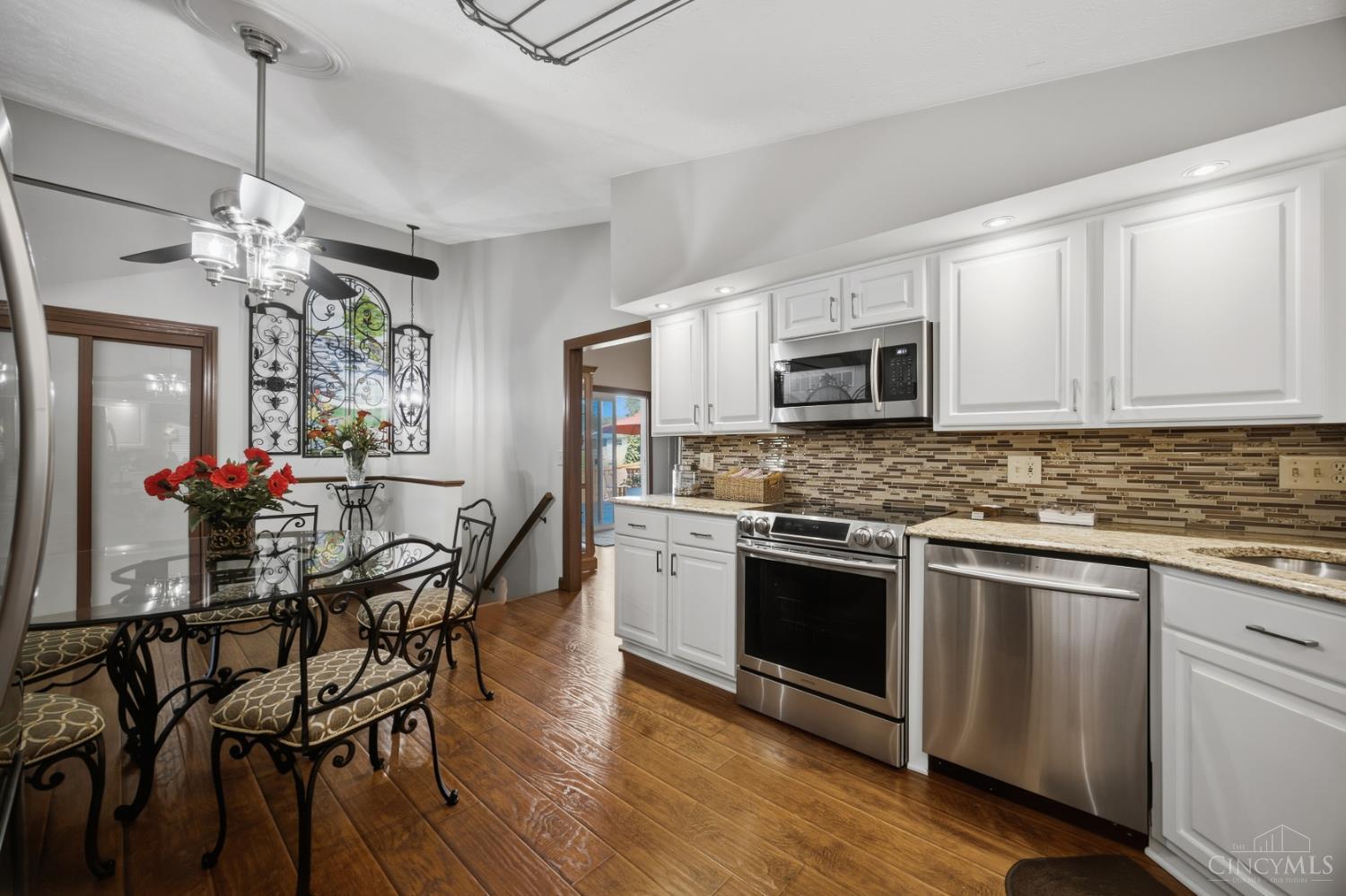 Kitchen with white cabinetry, stainless steel appliances, patterned backsplash, and a glass-top dining table.