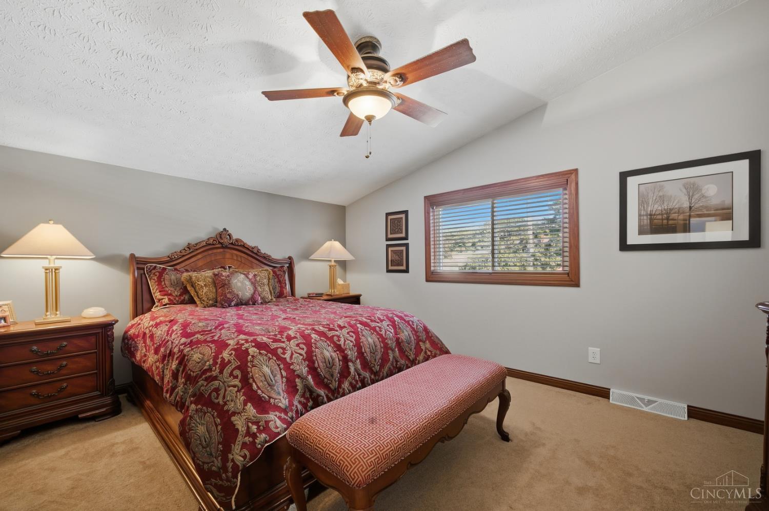 Furnished bedroom with a carved wooden bed, red patterned bedding, and a window with wooden blinds.