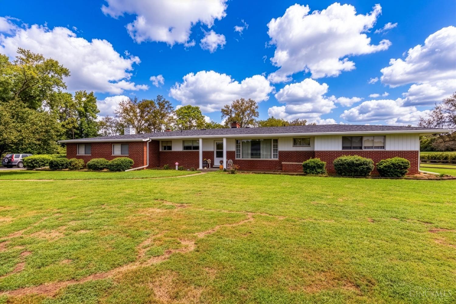Single-story brick ranch with white siding, trimmed shrubs, and a broad front lawn.