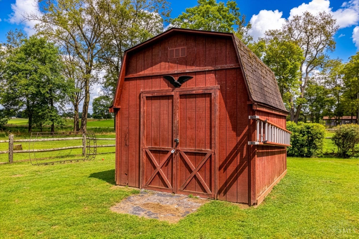 Red gambrel-roof barn with double doors on a fenced, tree-lined lawn.