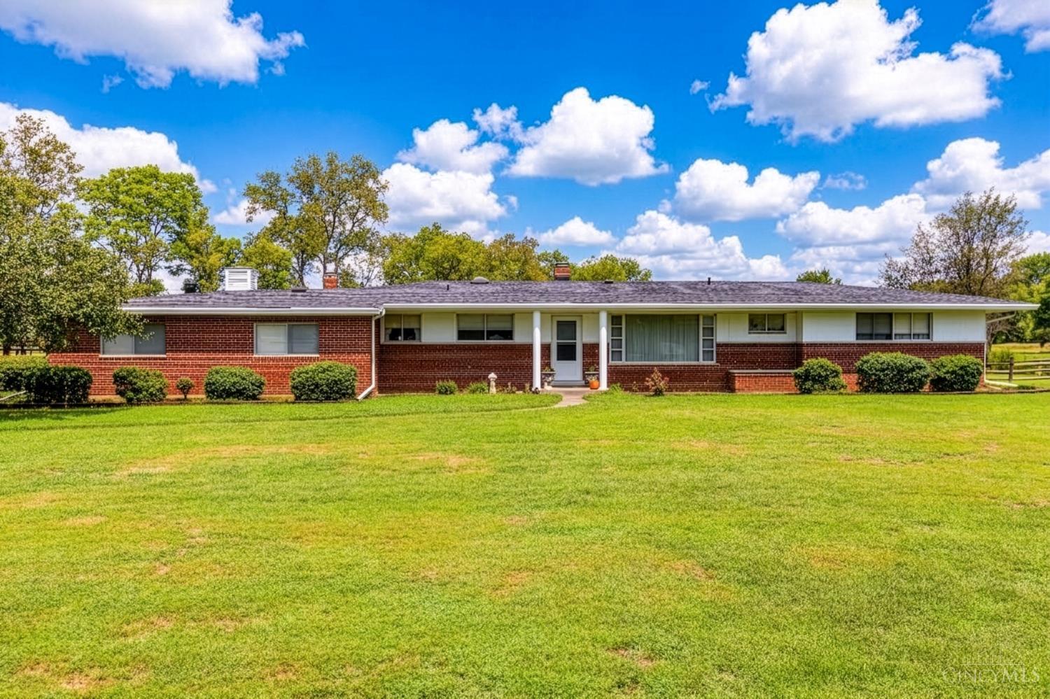 Single-story brick ranch house with white siding, front shrubs, and a broad green lawn.