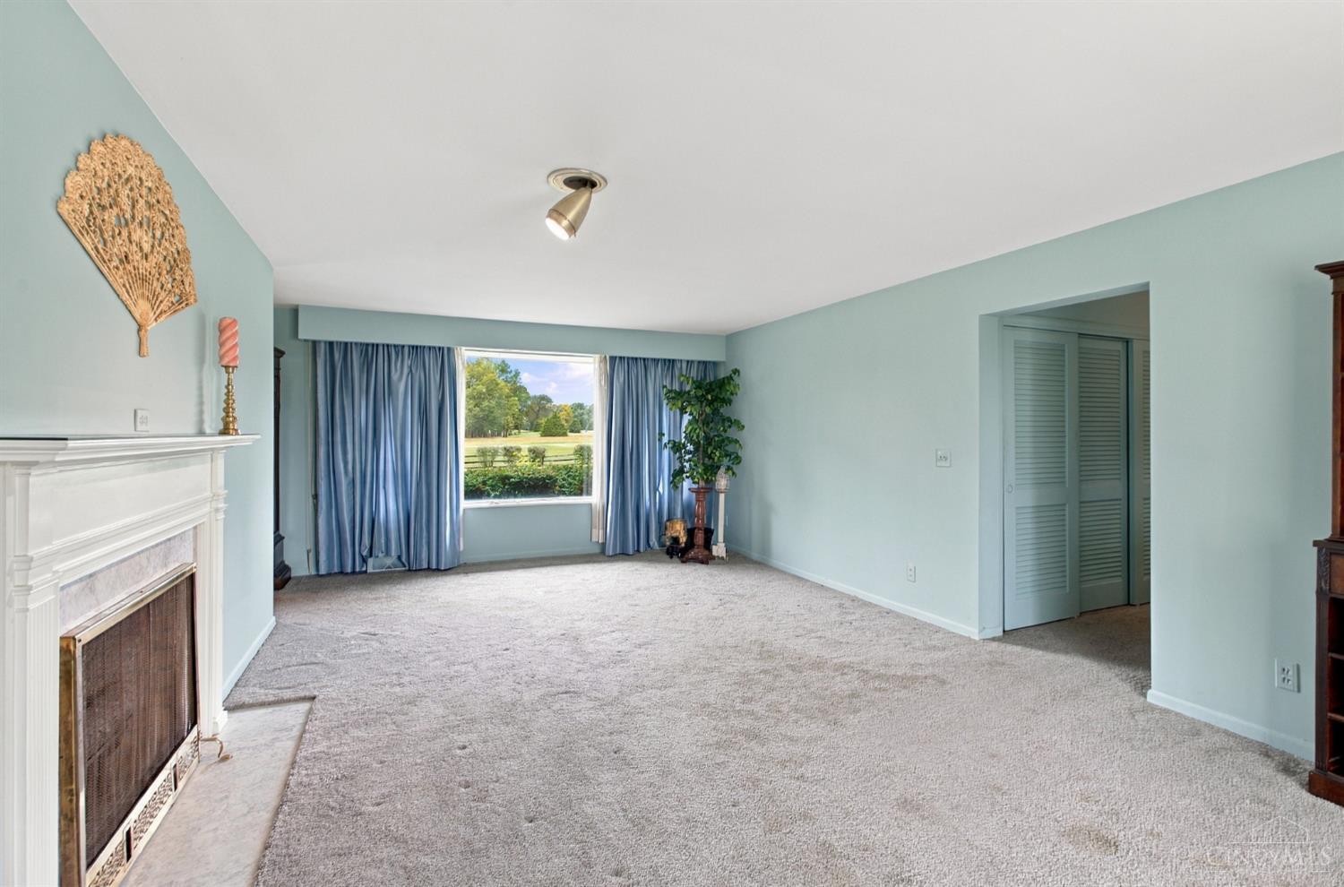 Living room with a white fireplace, blue curtains, and a large window overlooking a green lawn.