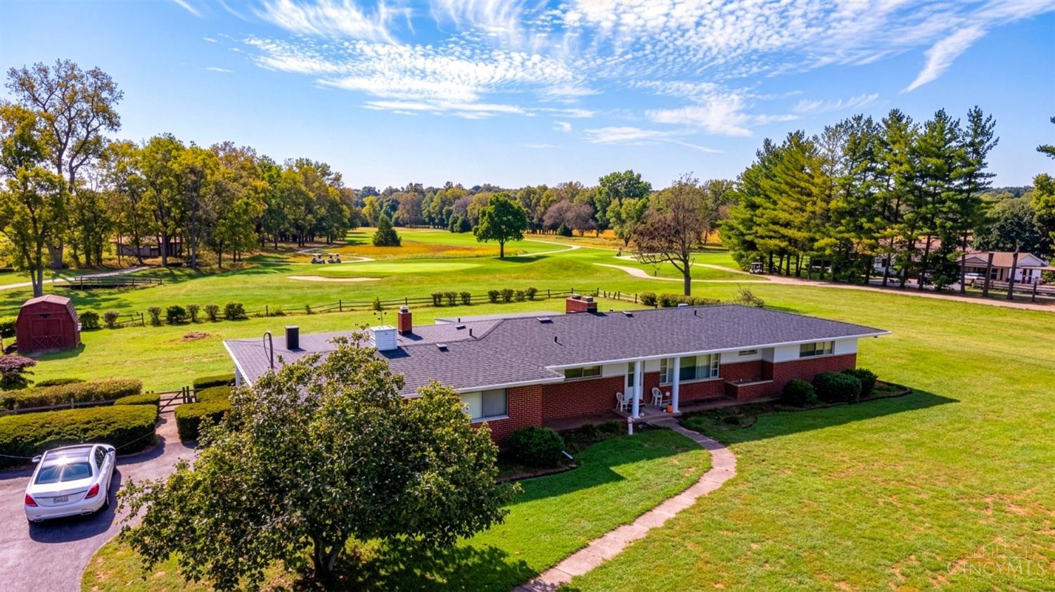 Aerial view of a brick ranch beside a golf course, with a broad lawn and mature trees.