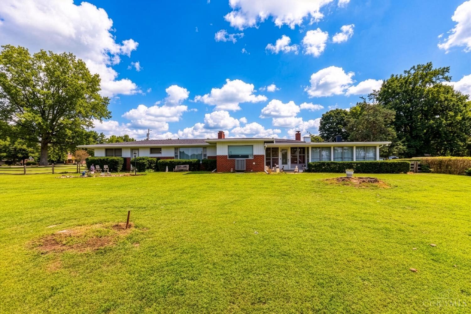 Single-story ranch home with red brick accents, a broad lawn, and mature trees.