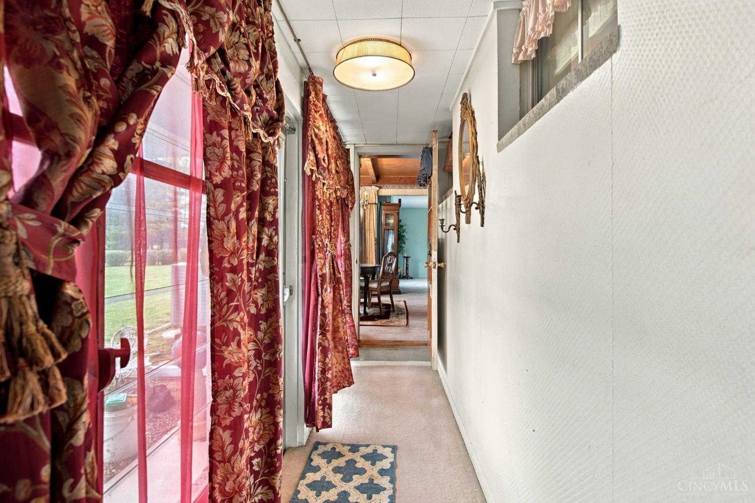 Carpeted hallway with ornate red curtains, tall windows, and mirrors along the wall.
