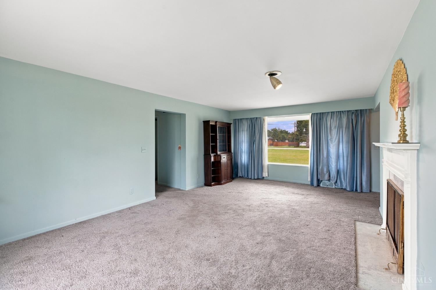 Living room with pale blue walls, wall-to-wall carpet, blue curtains, and a white fireplace.
