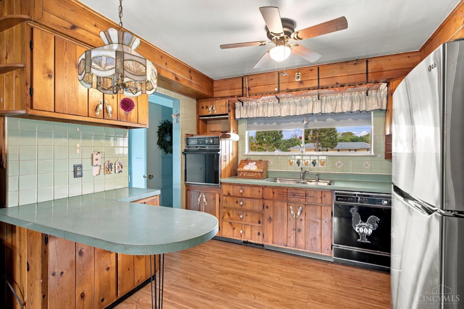 Kitchen with knotty wood cabinetry, pale green tile, rounded breakfast bar, and window above the sink.