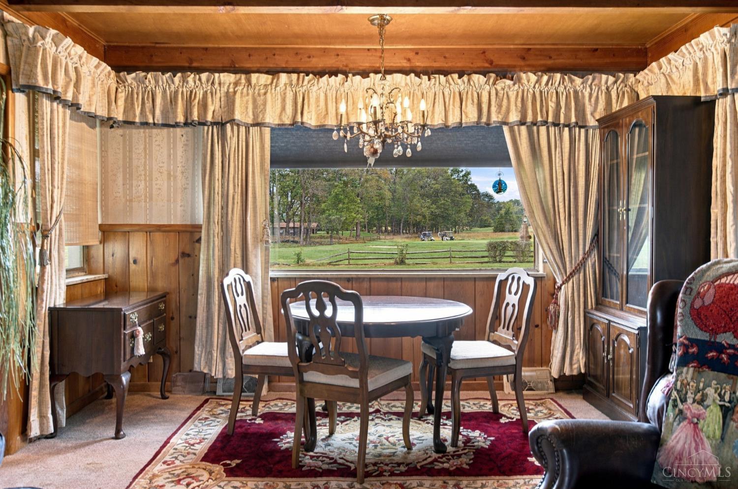 Wood-paneled dining room with an oval table and a large window overlooking a fenced lawn.