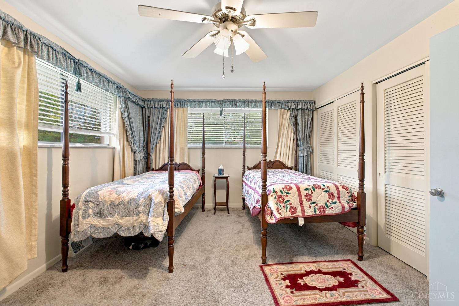 Bedroom with two four-poster twin beds, patterned quilts, and windows with blinds.