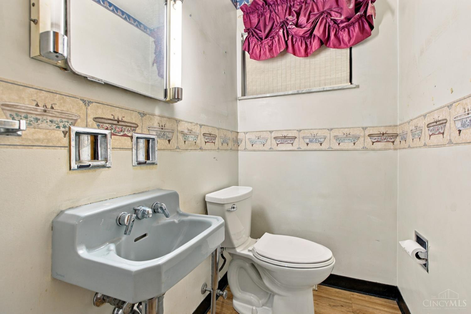 Bathroom with a gray wall-mounted sink, white toilet, patterned tile border, and magenta window valance.