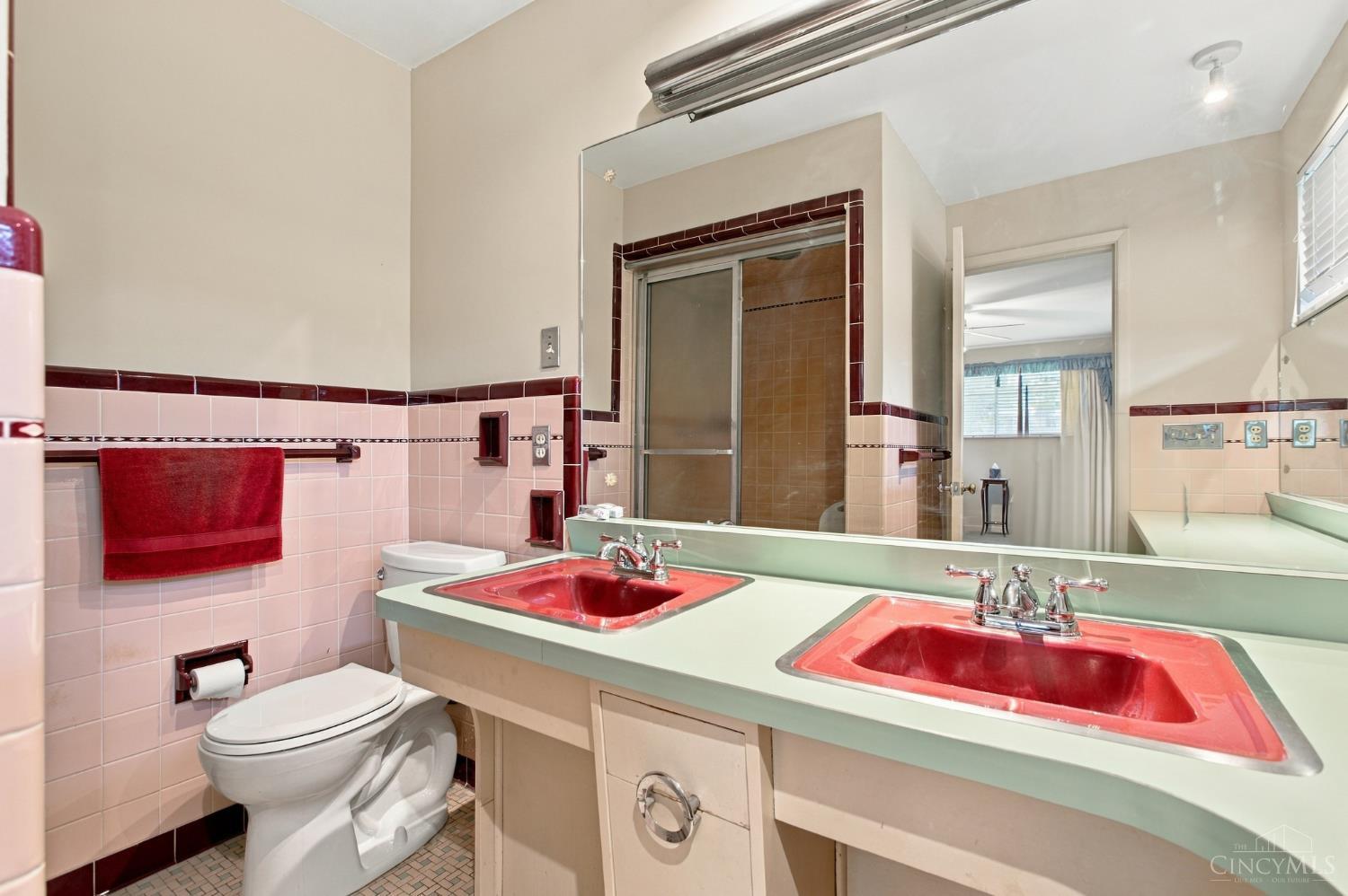 Bathroom with twin red sinks, a mirrored vanity, pink tile, and a glass shower.