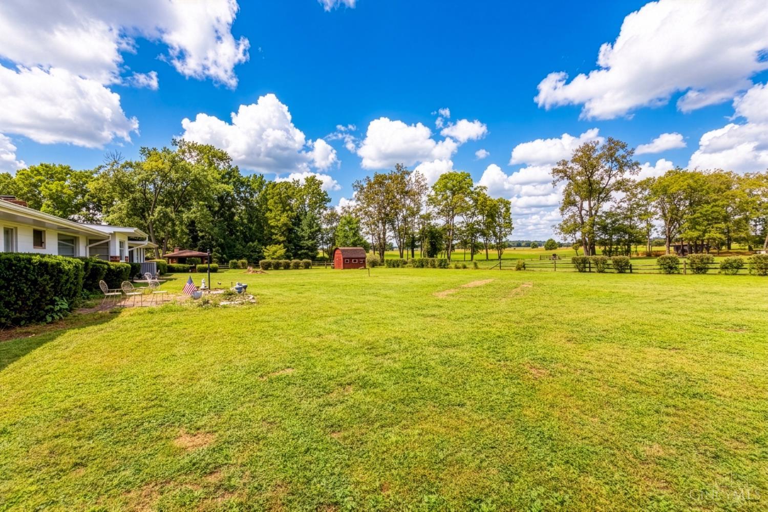 Expansive lawn with a small red barn, mature trees, and fenced fields behind the house.