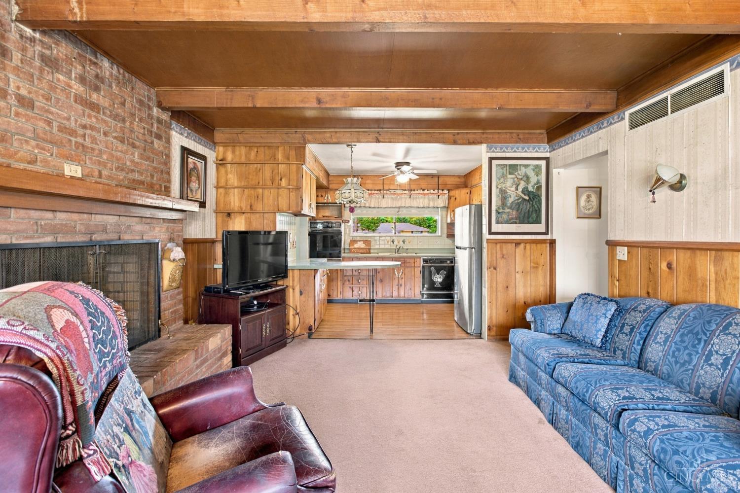 Living room with a brick fireplace and wood paneling, opening into the kitchen.