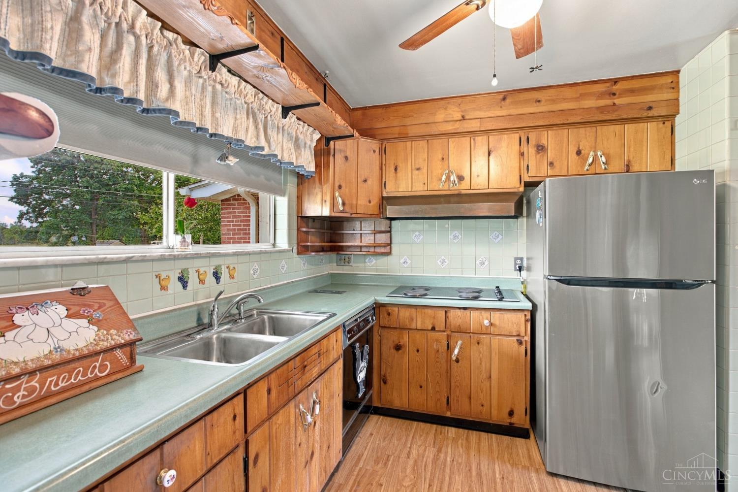 Kitchen with wood cabinets, pale green counters, a double sink, and a wide window.
