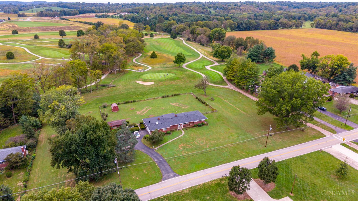 Aerial view of a brick home on a large lot beside a golf course and wooded hills.