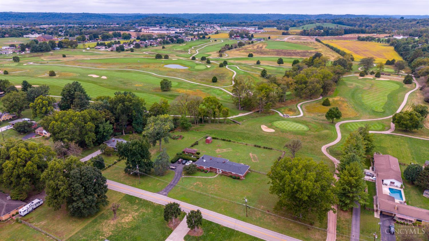 Aerial view of a brick ranch beside a golf course, with winding cart paths and wooded hills beyond.