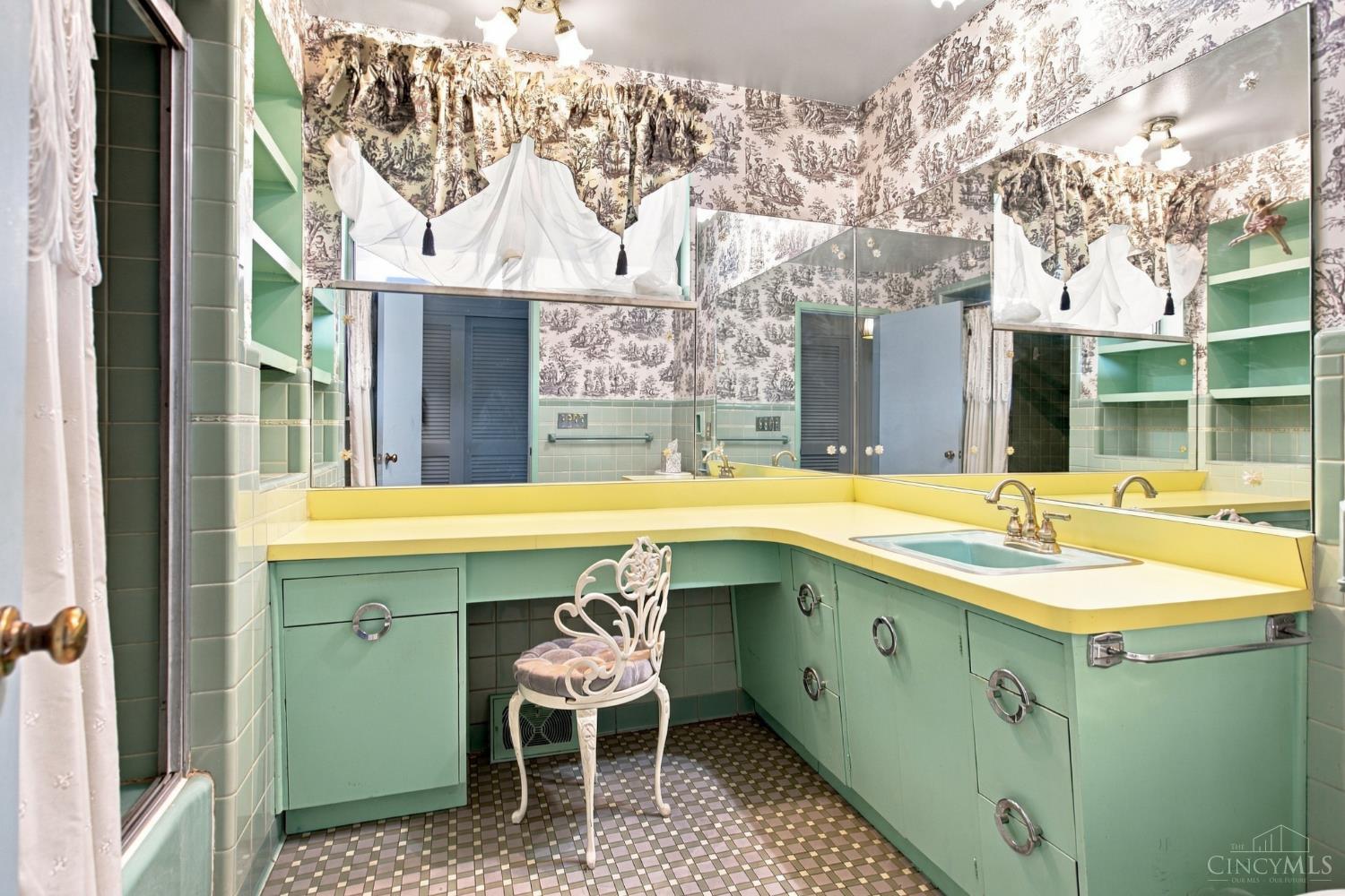 Bathroom with mint-green cabinetry, yellow counters, mirrored walls, and patterned toile wallpaper.