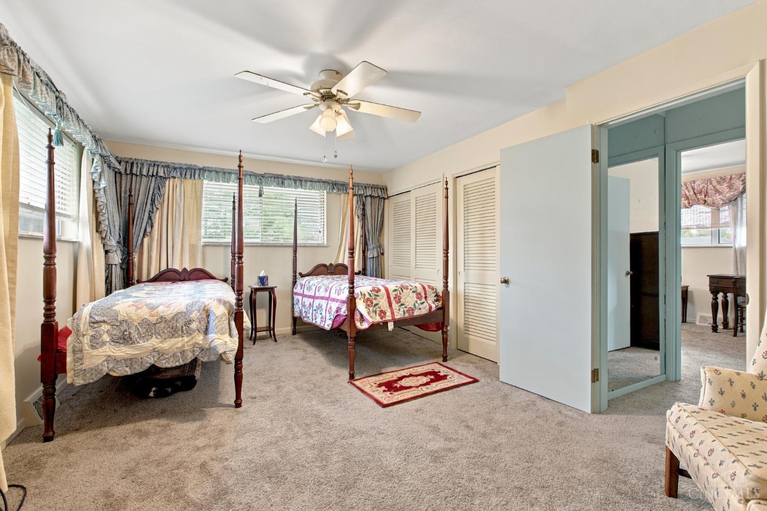Bedroom with two four-poster beds, floral bedding, beige carpet, and an open doorway to an adjoining room.