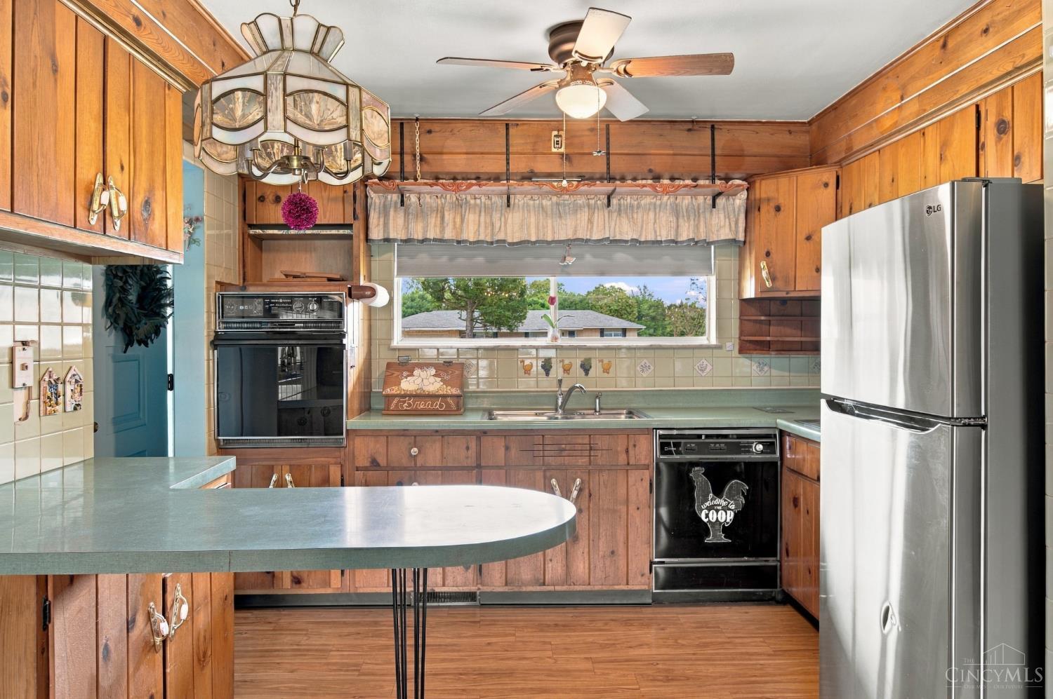 Kitchen with wood-paneled cabinetry, green countertops, and a wide window above the sink.