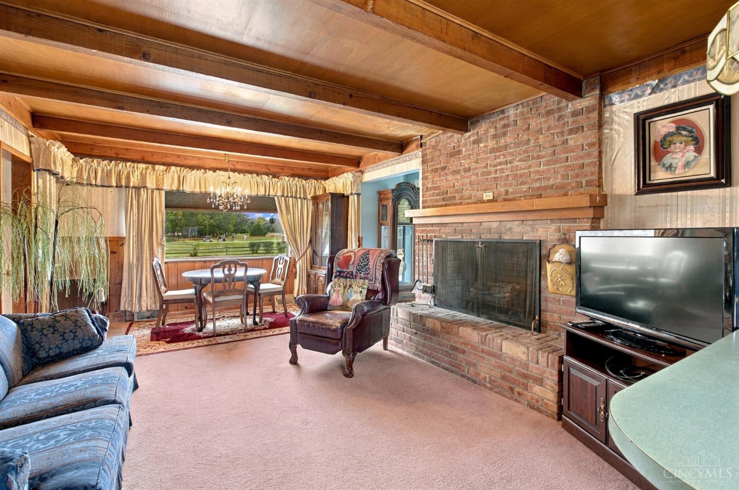 Living room with a brick fireplace, exposed wood beams, and a dining nook overlooking open fields.