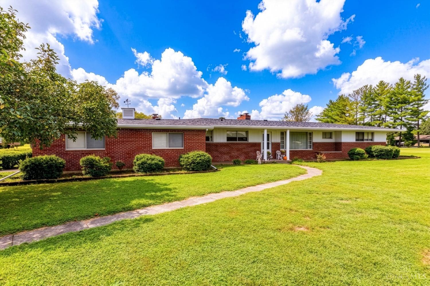 Single-story red brick ranch home with a covered entry, trimmed shrubs, and a curved walkway across the lawn.