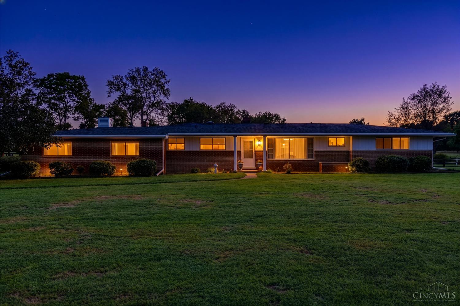 Single-story brick ranch with warmly lit windows and a broad lawn at dusk.