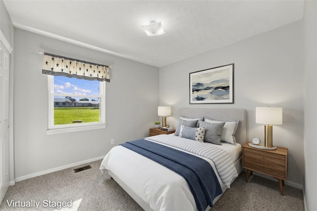 Bedroom with a neatly made bed, matching wooden nightstands, and a window overlooking a green lawn.