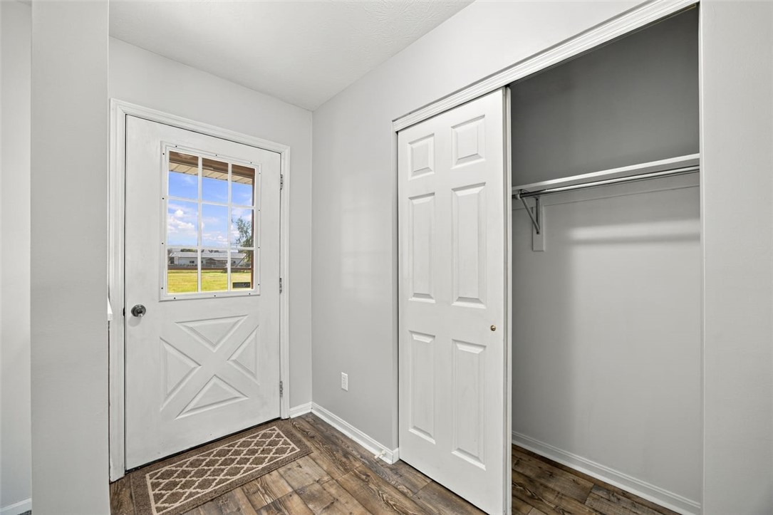 Entryway with a windowed white door, open closet, and wood-look plank flooring.
