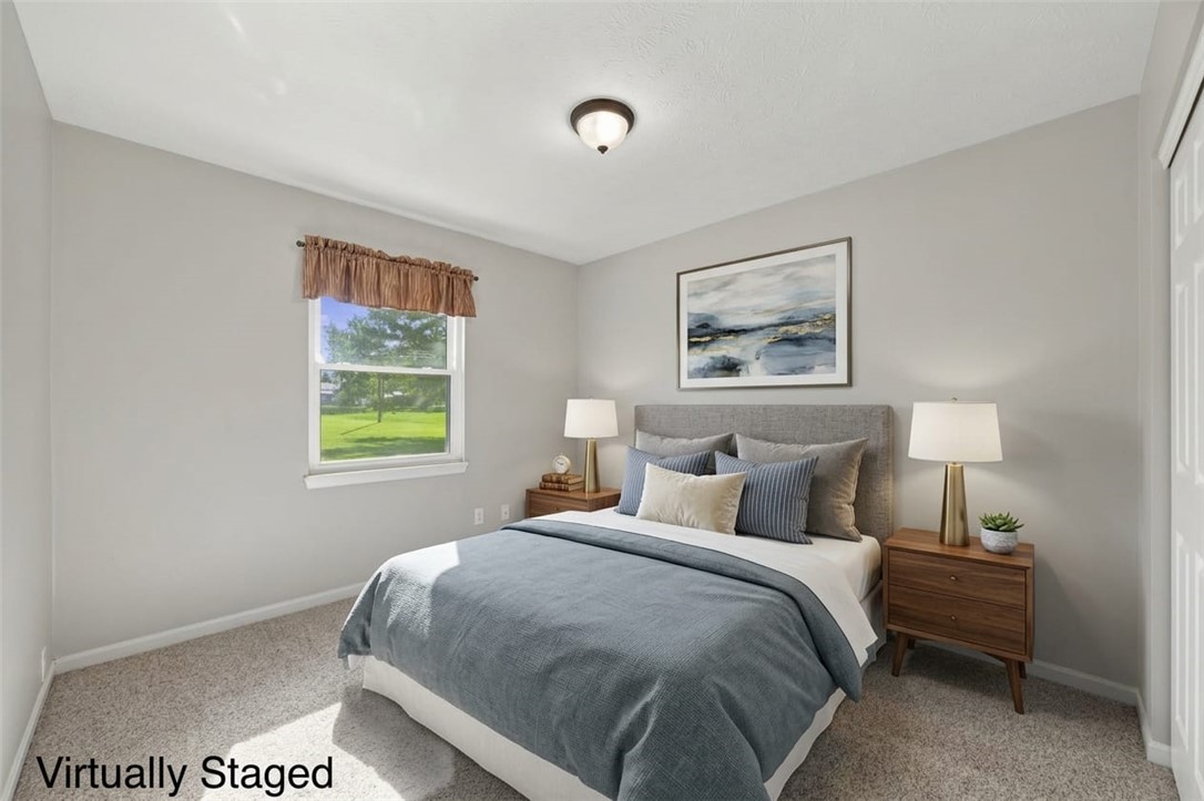 Bedroom with a gray upholstered bed, matching wooden nightstands, and a window overlooking a green lawn.