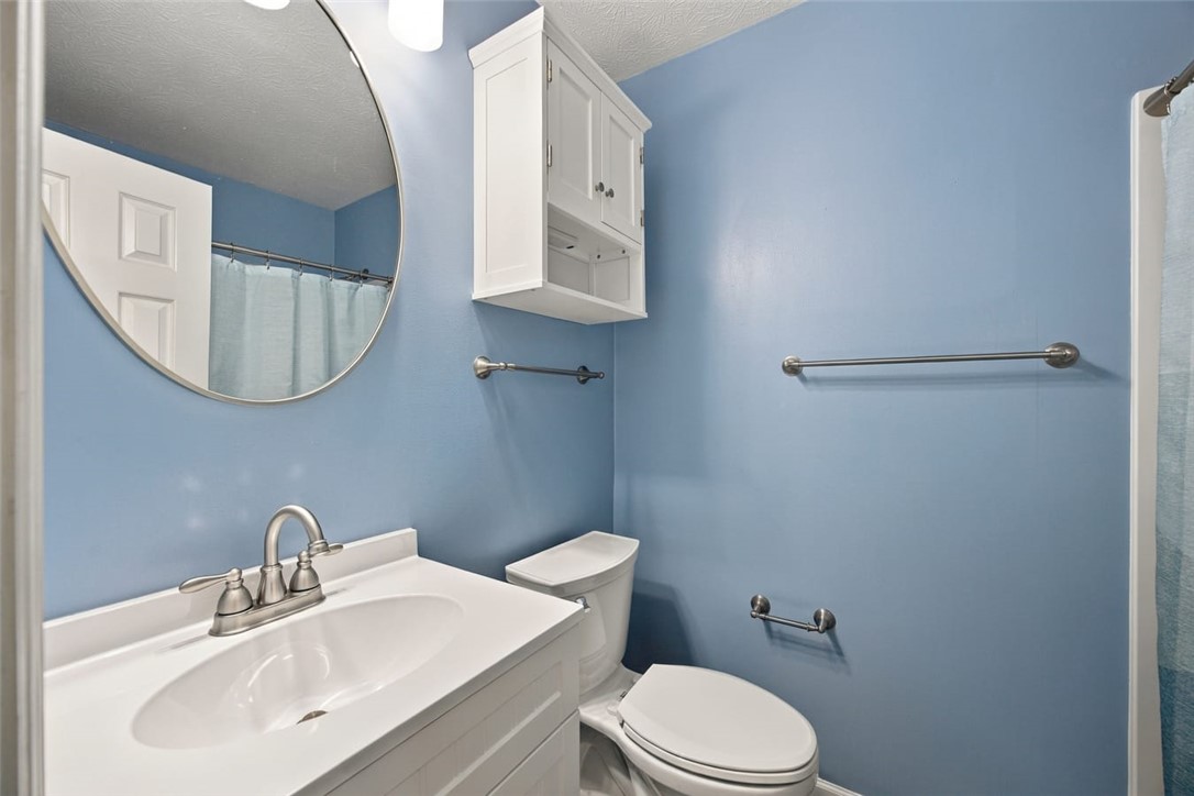 Bathroom with blue walls, white vanity, round mirror, toilet, and wall-mounted storage cabinet.