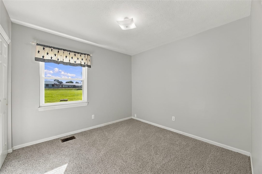 Vacant carpeted room with gray walls, a star-patterned window valance, and a view of a green lawn.