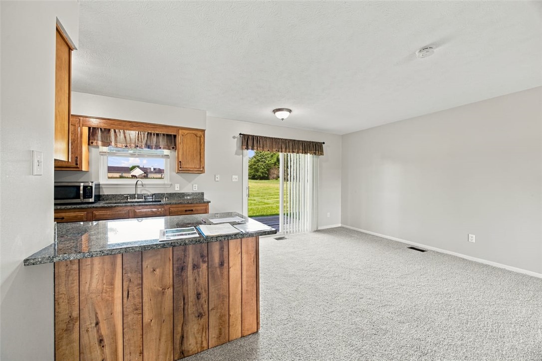 Unfurnished kitchen with wood cabinets and granite counters opening to a carpeted room and sliding glass door.